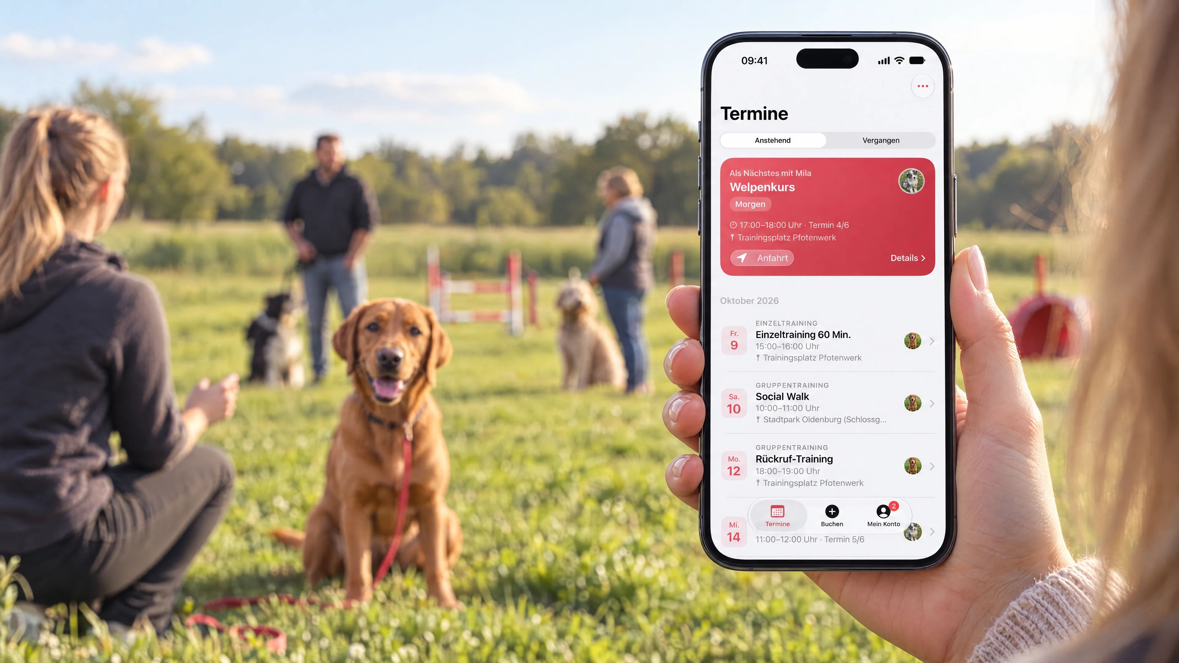 Hand hält ein iPhone mit der Terminübersicht der Hundeschule, im Hintergrund ein Gruppentraining auf der Wiese
