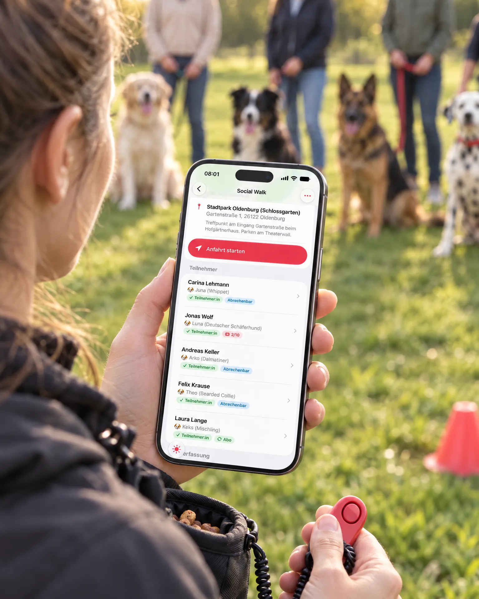Trainerin hält ein iPhone mit der Teilnehmerliste eines Social Walks, Hunde sitzen im Hintergrund